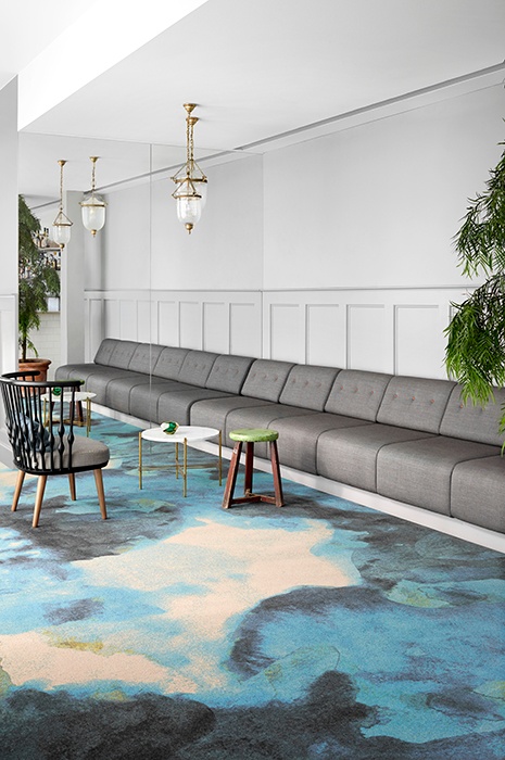 Fields of flow wall to wall carpet in cosy settings Einladende und helle Sitzecke mit grauen Sofas und auffallend bunten Teppichbahnen