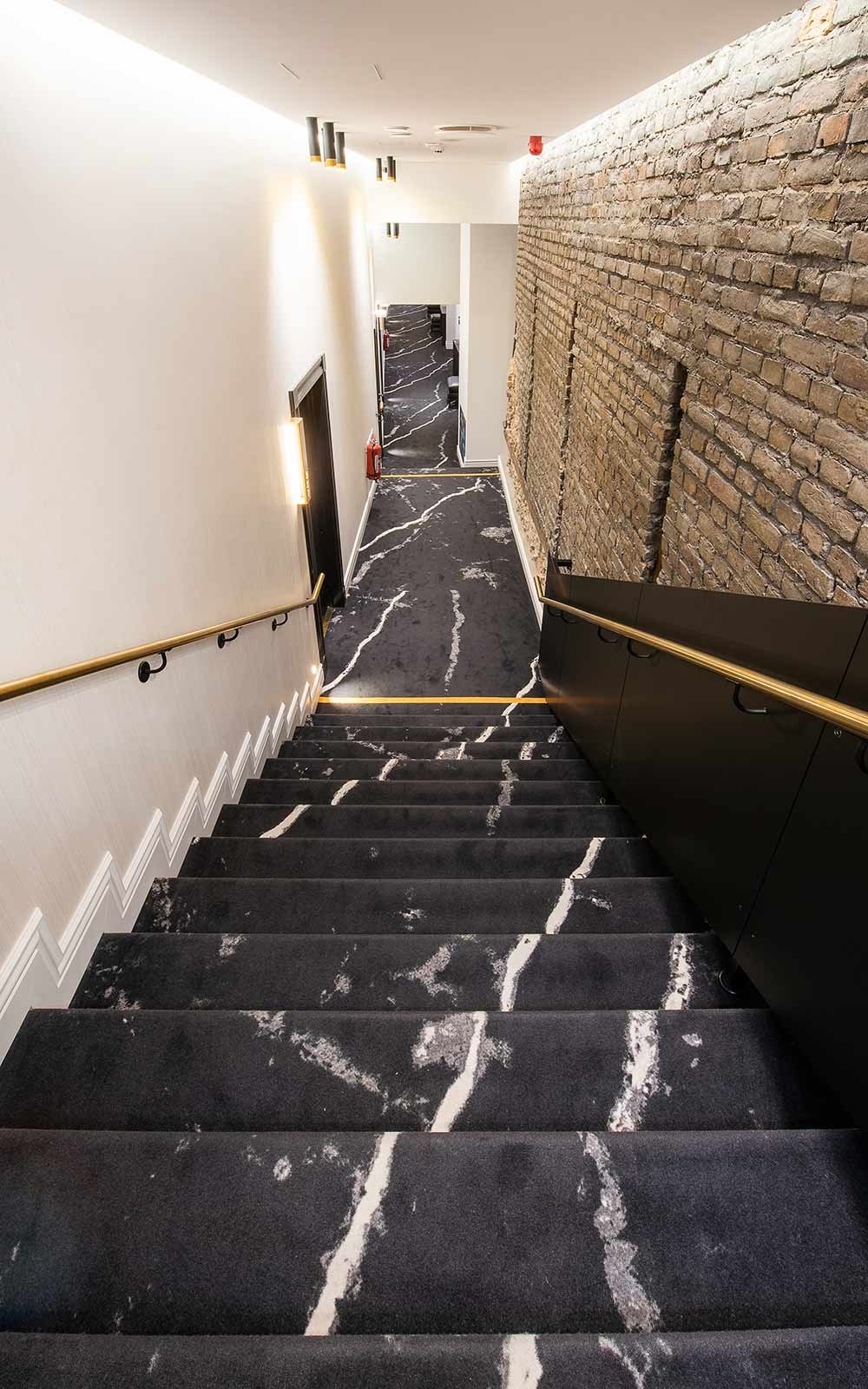 Hotel Teppichboden: Hotelflur mit Teppichboden in Marmoroptik, goldenen Raumakzenten und gemauerter Wand